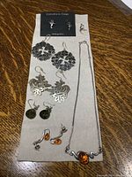 Full overview of 5 earring pairs and one necklace with pendant on cream background.