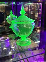Photo of the green uranium glass candy dish glowing under black light in a display cabinet.