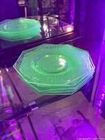 Five stacked small octagonal uranium glass plates glowing bright green under UV light, showing texture and edges clearly.