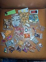 Multiple resealable bags of various beads in different shapes, sizes, and colors on a brown chair.