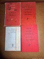 Four books stacked and arranged showing front covers: three red "New Basic Course in Pitman Shorthand" titles and one white "Student's Shorthand Dictionary - Phrase Book" cover, showing wear and markings.