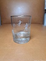 Front view of the glass showing etched figure skaters and the Olympic torch design, along with textured concave base.