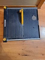 Top-down view of the Mastercraft wet tile saw showing the ribbed black surface, yellow saw blade, yellow handle, and measurement markings.