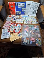 Top-down view of vintage stamps collection including albums, loose stamps, mounted sheets, and collecting pamphlets spread on an armchair