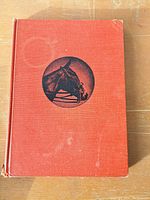 Front cover of the Riding by Benjamin Lewis book showing reddish-orange cloth cover with black round horse illustration.