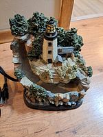 Side view of the lighthouse water fountain showing rocky base, stairs, lighthouse building, and surrounding trees