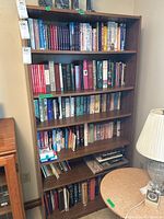 Photo showing full wooden bookcase with 5 shelves filled with assorted books of different sizes and colors