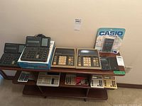 Photo of calculators arranged on a wooden shelf, showing a variety of brands and styles.