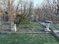 View of four concrete planters arranged outdoors by garden beds with some visible wear and cracks, surrounded by wood rail borders and leaf litter.