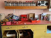 Wide shot of the yellow workbench, shelf with jars, and various tools and accessories on the bench top.