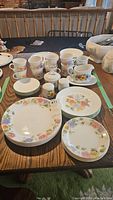 Full view of dinnerware set laid out on table showing plates, cups, creamer, sugar bowl, and saucers with floral pansy designs.