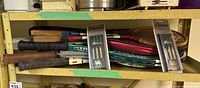 Full view of two packs of Wiftflyte darts in plastic packaging and vintage wooden and metal tennis and badminton rackets stacked behind them on a shelf.
