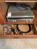 Vintage Fisher Studio-Standard AM/FM receiver unit placed on wooden shelf with power cord on top and stereo hookup cables organized inside the drawer below.