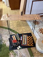 Overview of oversized wooden cribbage board with metal legs and multiple games below