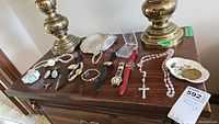 Photo shows an array of ladies watches, necklaces including a rosary, earrings, a bracelet, and a Coalport china ring dish on a wooden surface.