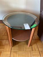 Front perspective showing glass top, wood legs, and lower circular wood shelf.