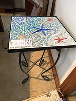 Side table with mosaic tile starfish top and scroll metal base, viewed from front angle.