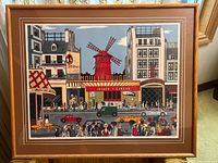 Framed lithograph showing a vibrant street scene centered on Moulin Rouge with a red windmill and crowds of people.