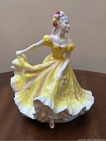 Front angle showing yellow dress with pink floral decoration and white ruffled skirt on porcelain figurine
