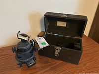 WWII Mark II Astro Compass displayed beside its open wood carrying case with metal latch, showing the interior compartment.