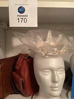 Two medium-sized handbags placed next to a white styrofoam mannequin head wearing a soft pearl adorned crown.