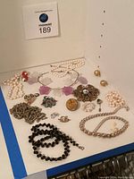 View of assorted jewelry showing pearl necklaces, brooches, rings, earrings, and pins on white surface.