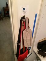 Photo showing 2 handbags/travel bags hanging, one red with black strap and one beige/tan money belt or strapped item