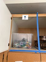 Clear plastic bin holding assorted Mardi Gras bead strands in various colors inside a wooden cabinet.