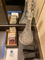 Photo of large cut crystal spirit decanter with stopper, two black resin KEM card holders, and multiple decks of cards in cardboard box.