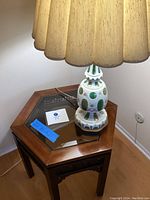 Full view of hexagonal side table with glass top and porcelain lamp with pleated beige shade.
