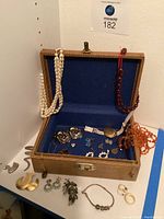 Full view of open tweed-style jewelry box on shelf with necklaces hanging over lid and jewelry displayed inside and in front