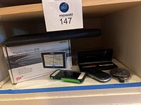Photo of Magellan Maestro 4250 GPS box with flip phone, iPhone, fountain pen case, earbuds, and folder on shelf