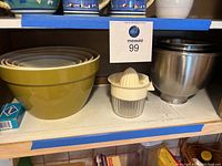Plastic nested mixing bowls in green and white, metal juicer with cream handle and base, stainless steel KitchenAid mixing bowl.