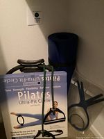 Photo showing Pilates Ultra-Fit Circle box with resistance band and handle attached, rolled blue exercise mat behind it.