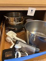Mixed stainless steel and black pots, large metal mixing bowl, and various Pampered Chef kitchen tools grouped together.