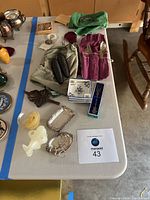 Multiple assorted decorative items arranged on a white table including silver trays, porcelain dishes, cutlery sets in fabric rolls, pinecone objects, candle, marble elephant figurine, and wooden decorative piece.