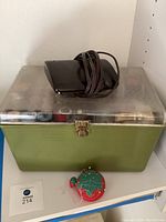 Large green sewing box with metal rim and a black sewing machine foot pedal on top.