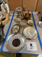 Overall lot showing various silver serving dishes, candy dishes, wooden parrot figurine, and other items on table.