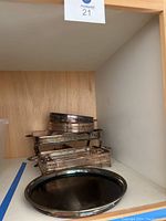 Various rectangular and round silver serving holders stacked inside a wooden shelf space.