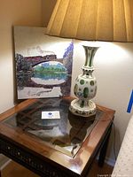 Photo of side table with lamp atop and painting leaning against wall