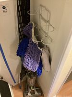 Hoover Air vacuum and two white metal push mop frames with multiple microfiber pads in purple and blue hanging on wall hooks.