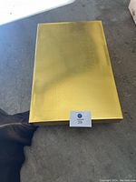 Golden colored box or item unrelated to the dress, flat on a grey surface.