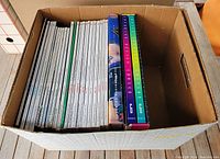 Box containing 23 white spine architectural magazines with two sets of three colorful hardcover Interior Design books in slip cases on the right side.