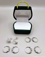 Photo showing four pairs of silver earrings arranged with a jewelry box in the background, featuring various hoop designs including twisted and knotted wire patterns.