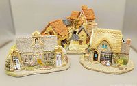 Front view of three ceramic cottages showing detailed roofs, doors, windows, and small painted figure accents.