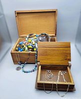 Two wooden jewellery boxes open showing multiple costume bead necklaces and two silver chains.