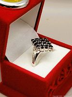 Square cluster black sapphire silver ring shown from an angle in a red velvet box with white interior.