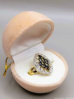 Silver ring marked 925 in an oval design with marquise-cut dark blue sapphires set in gold-tone and silver-tone detailed setting inside a beige velvet display box.