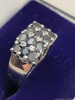 Close-up image of the ring face showing rectangular cluster of grey sapphires and smaller white stones in a grid pattern on silver band.