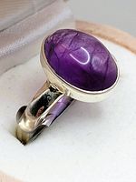 Close-up view of sterling silver ring with large oval violet amethyst cabochon showing natural inclusions and smooth bezel setting.